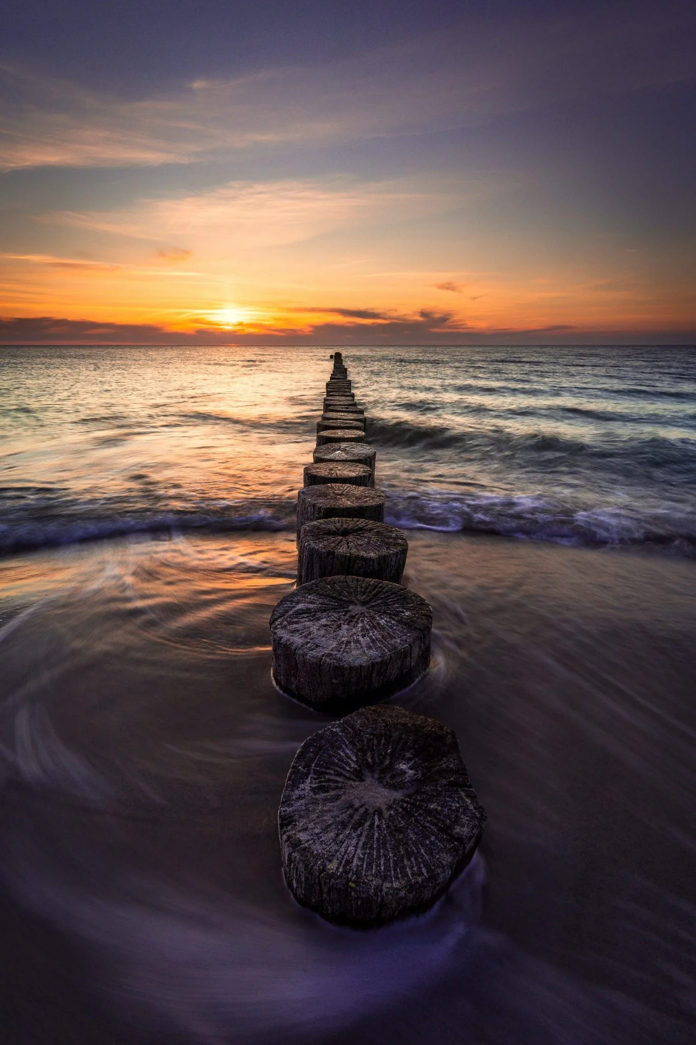 Wooden stepping stones leading out into the sea at sunset